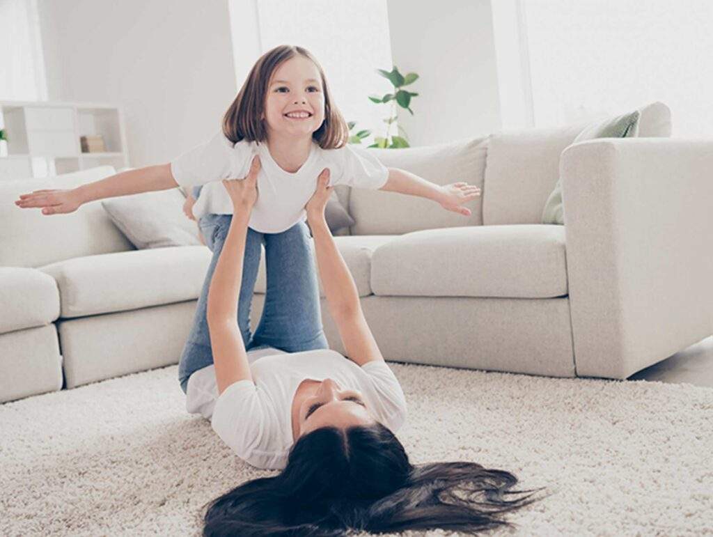 Lady laying on carpet in a living room holding up her daughter